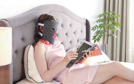 a woman reading a magazine while wearing a red light therapy mask